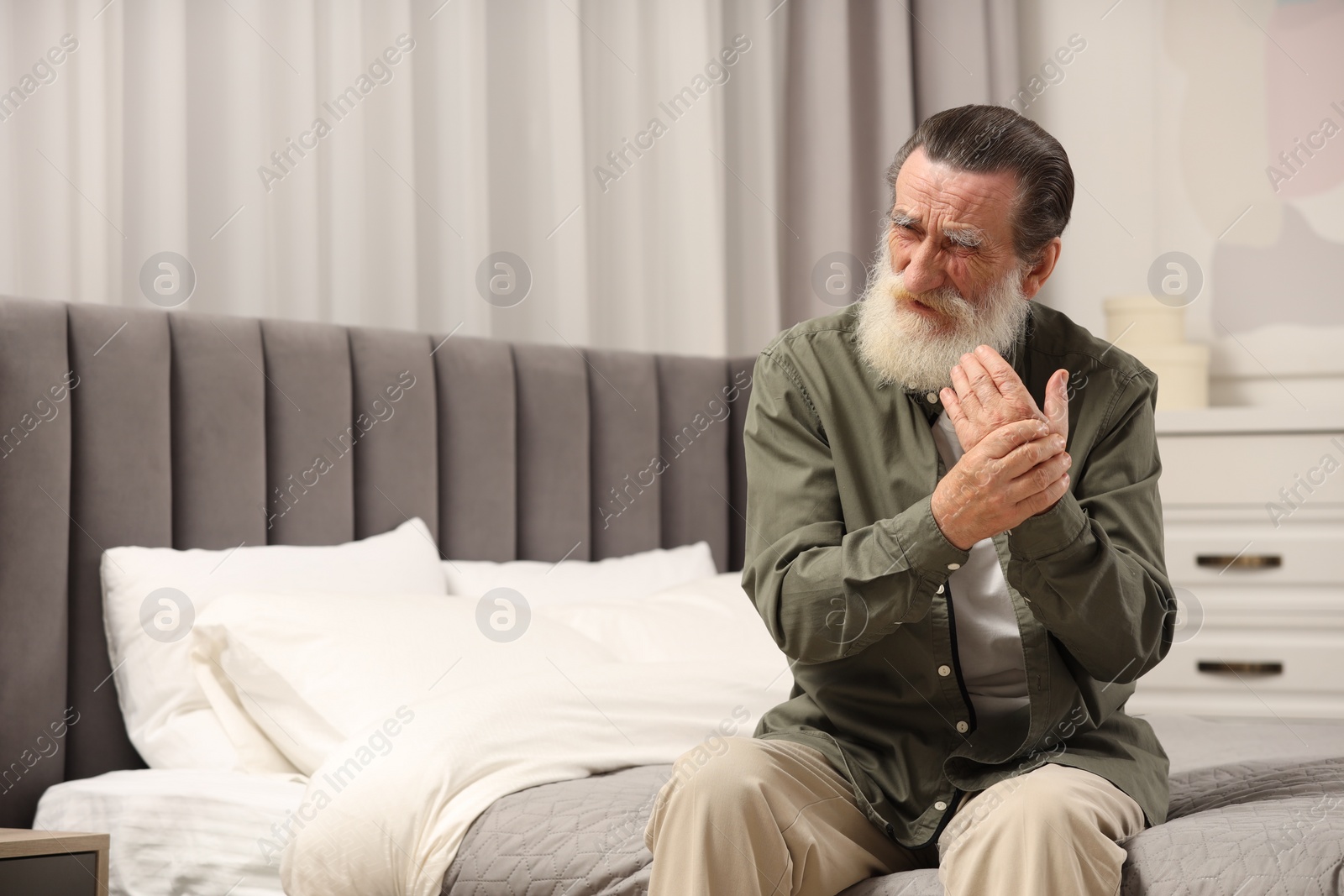 Photo of Senior man suffering from pain in hand on bed at home. Rheumatism symptom