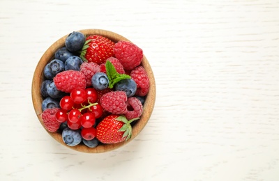 Photo of Mix of different fresh berries in bowl on white wooden table, top view. Space for text