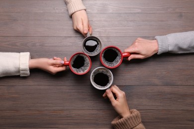 Photo of Women with cups of coffee at wooden table, top view