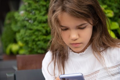 Teenage girl using smartphone in outdoor cafe, space for text