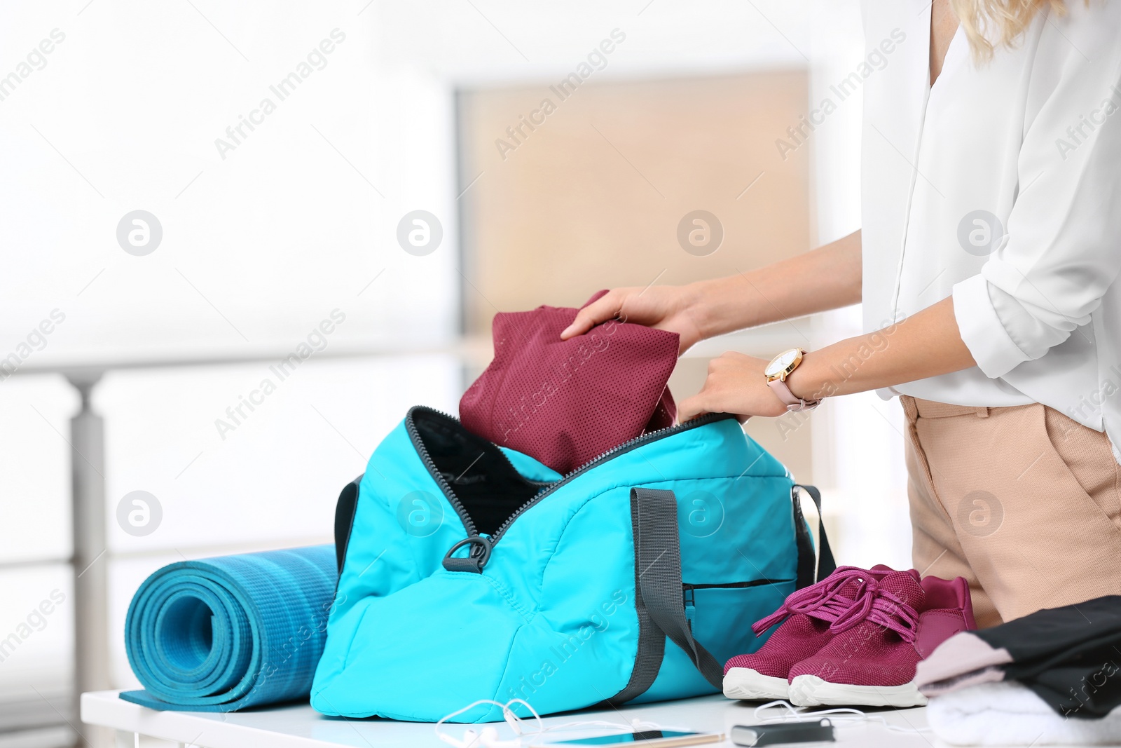 Photo of Young businesswoman packing sports stuff for training into bag in office