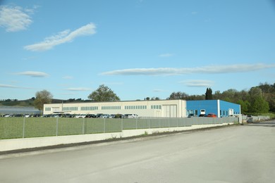 Photo of Factory building with parking lot surrounded by fence on sunny day