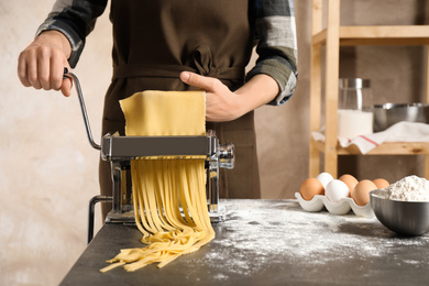 Woman preparing noodles with pasta maker machine at table indoors, closeup