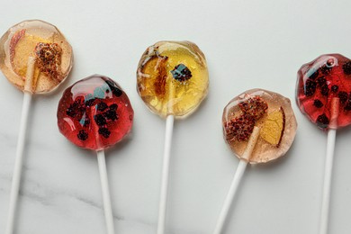 Sweet colorful lollipops with berries on white marble table, flat lay