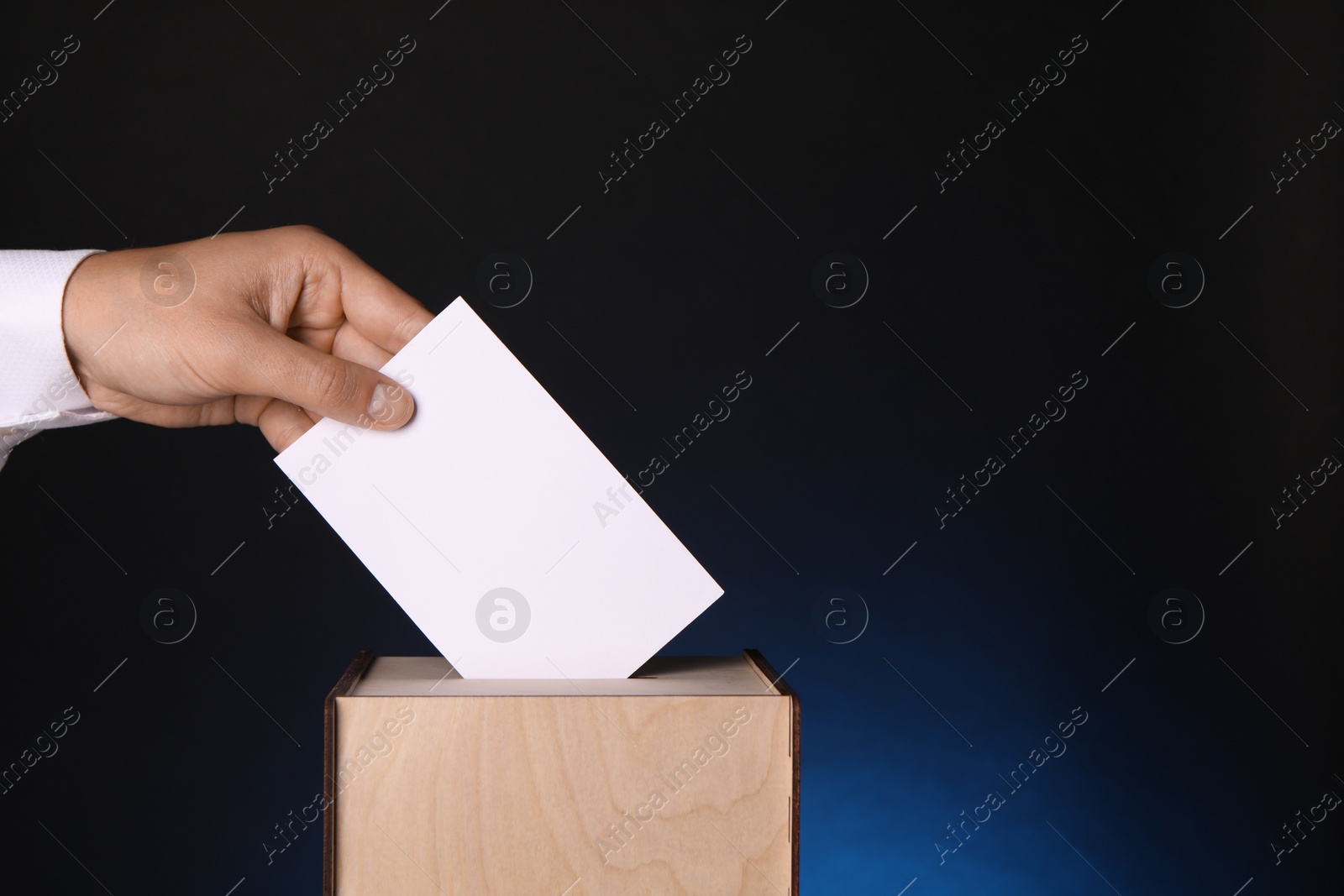 Photo of Man putting his vote into ballot box on dark blue background, closeup. Space for text