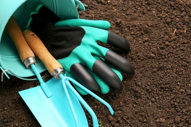 Photo of Overturned bucket with gardening tools and gloves on fresh soil. Space for text