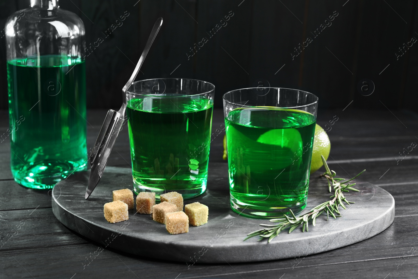 Photo of Absinthe in glasses, rosemary, brown sugar and lime on black wooden table. Alcoholic drink
