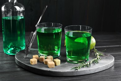 Photo of Absinthe in glasses, rosemary, brown sugar and lime on black wooden table. Alcoholic drink