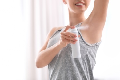 Beautiful young woman applying deodorant in room