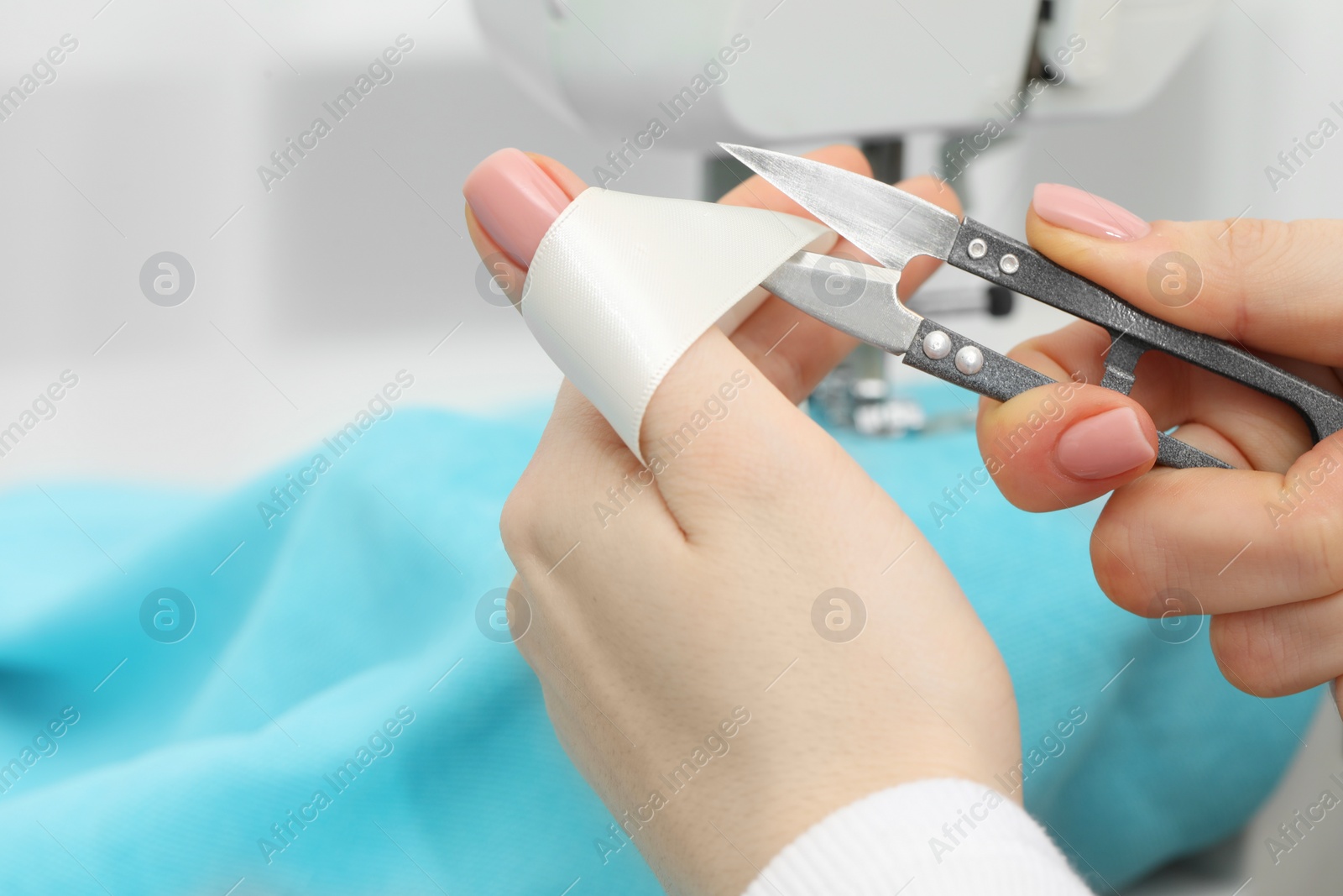 Photo of Seamstress with tailor's scissors working with sewing machine indoors, selective focus