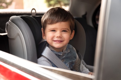 Cute little child sitting in safety seat inside car. Danger prevention