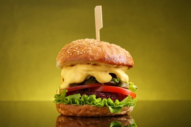 Photo of Delicious vegetarian burger on mirror surface against olive background