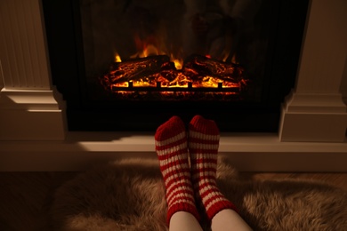 Photo of Woman in warm socks resting near fireplace with burning woods indoors, closeup