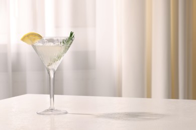 Photo of Elegant martini glass with fresh cocktail, rosemary and lemon slice on white textured table indoors. Space for text