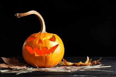 Photo of Halloween pumpkin head jack lantern on table against dark background with space for text