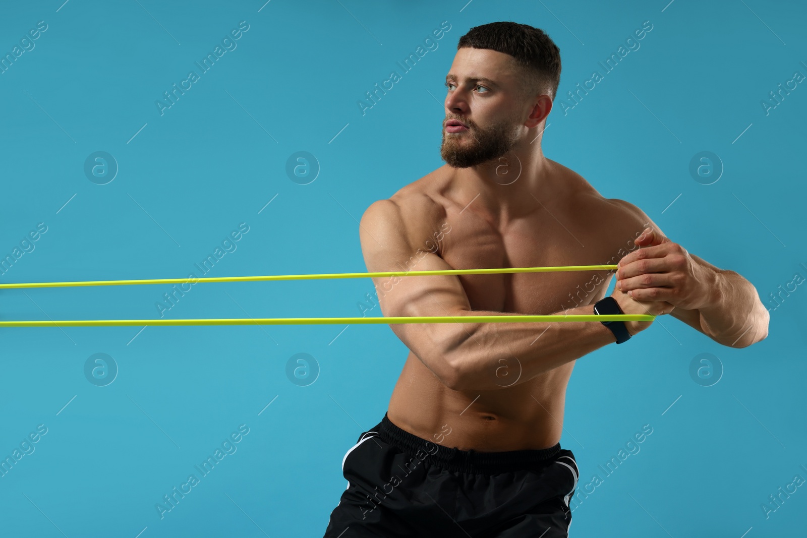 Photo of Muscular man exercising with elastic resistance band on light blue background