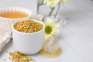 Photo of Fresh bee pollen granules and dipper with honey on white tiled table, closeup. Space for text