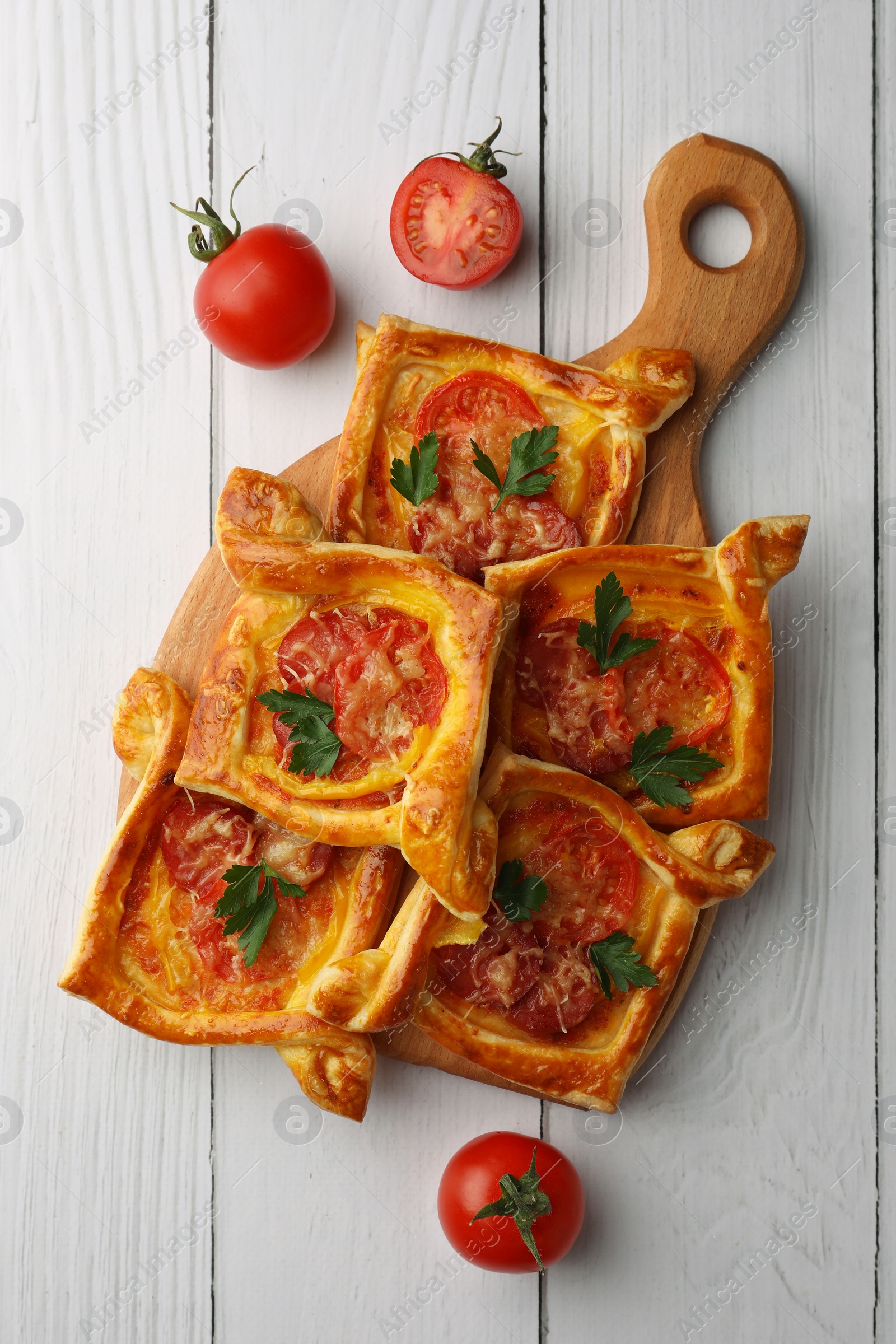 Photo of Fresh delicious puff pastry with cheese, tomatoes and parsley on white wooden table, flat lay