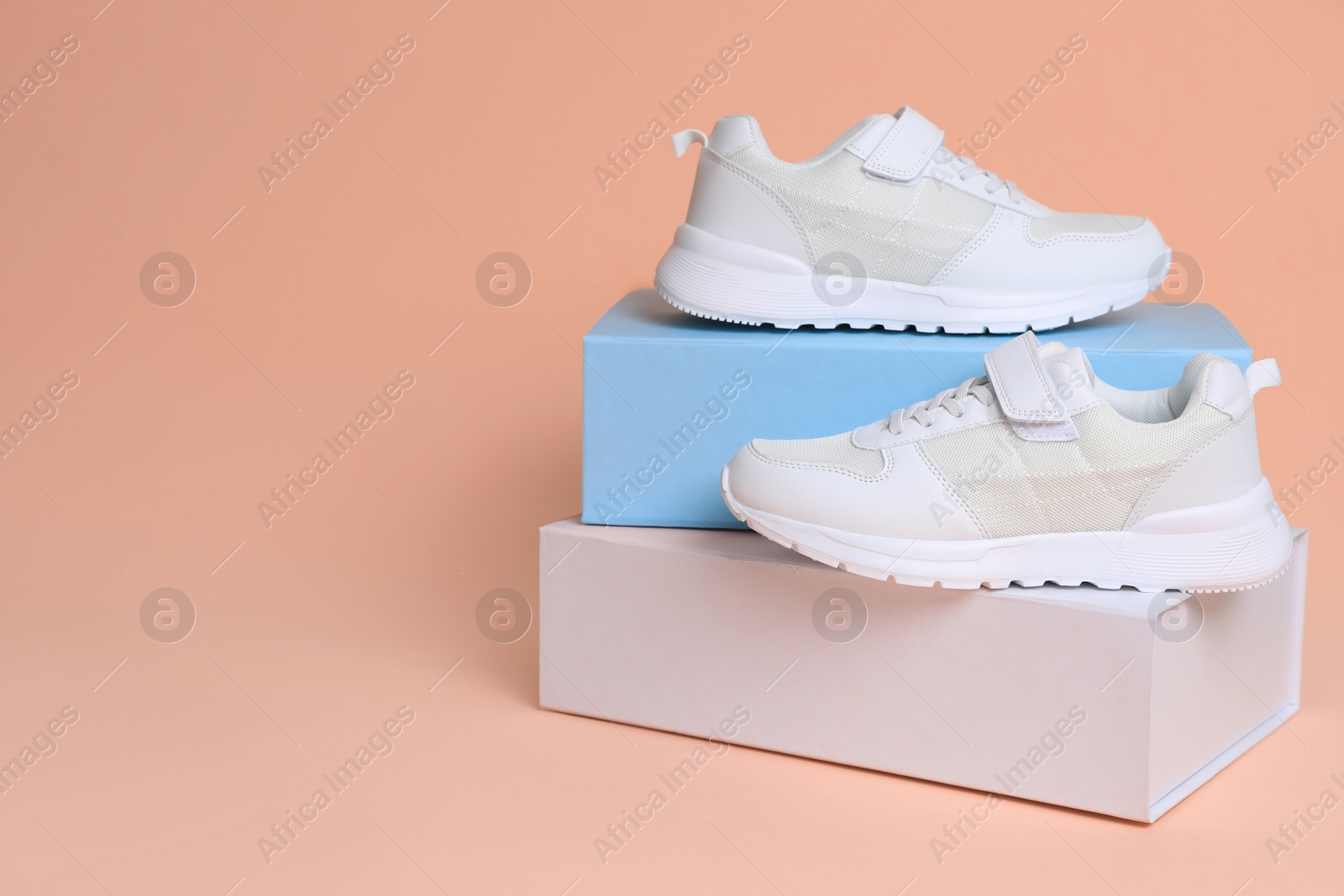 Photo of Pair of comfortable sports shoes and boxes on pale coral background. Space for text