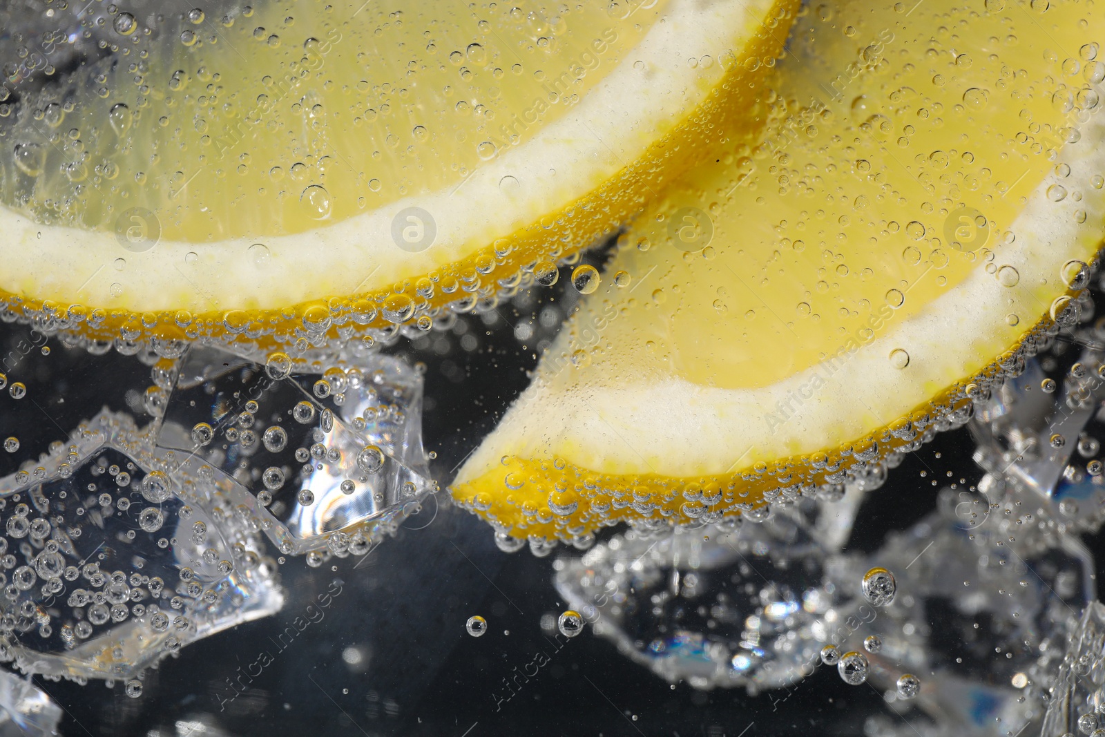 Photo of Juicy lemon slices and ice cubes in soda water against black background, closeup