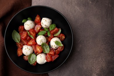 Tasty salad Caprese with tomatoes, mozzarella balls and basil on brown table, top view. Space for text