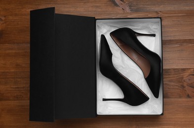 Photo of Pair of stylish shoes in black box on wooden background, top view