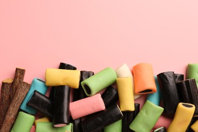 Many tasty candies and dried cut liquorice root on pink background, top view. Space for text