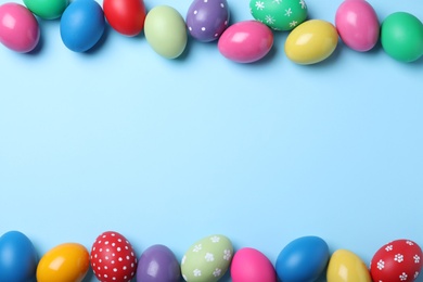 Photo of Bright painted eggs on light blue background, flat lay with space for text. Happy Easter