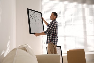 Photo of Man holding picture near white wall in room. Interior design