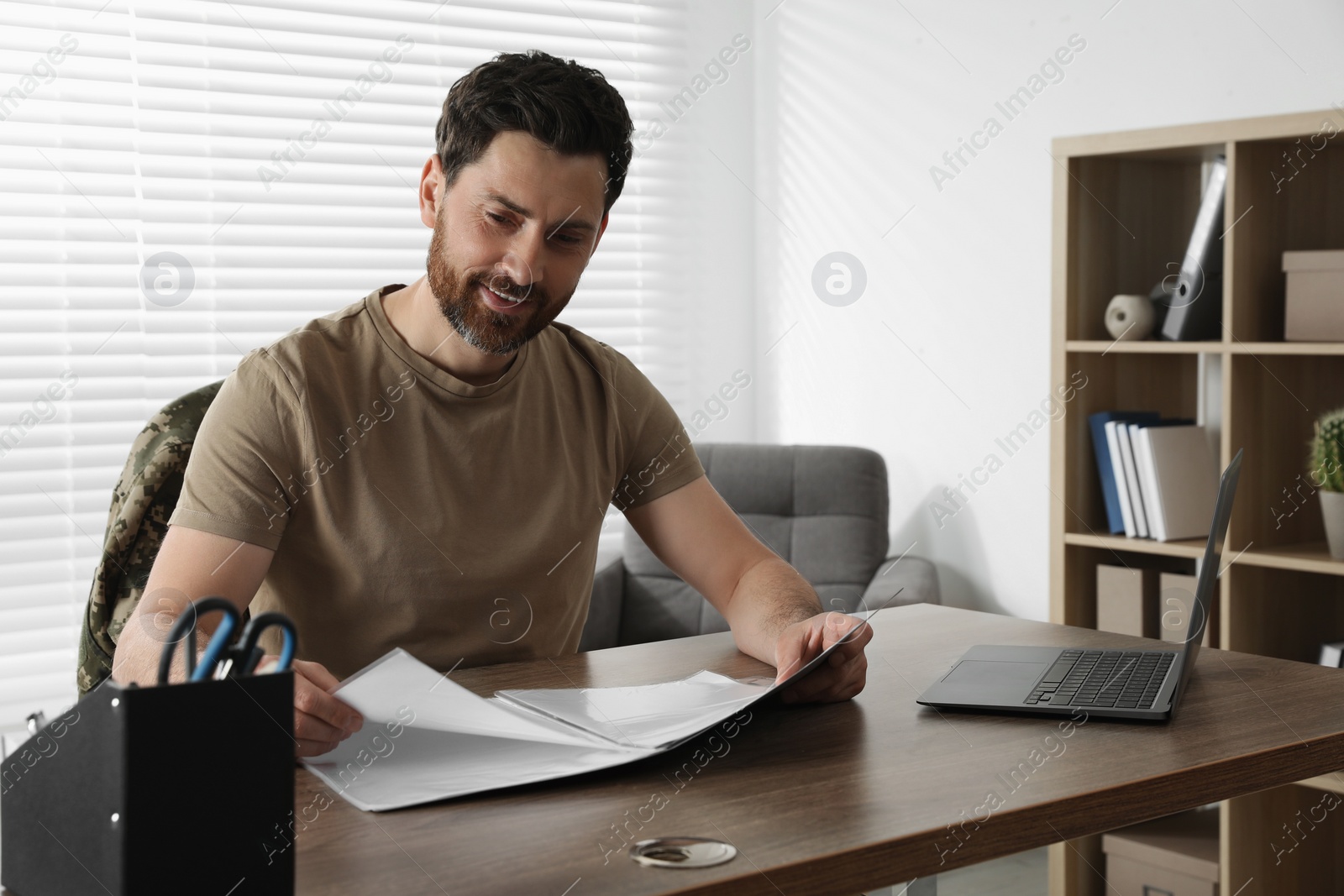 Photo of Happy soldier working with documents at wooden table indoors. Military service