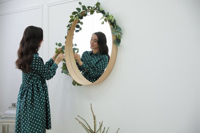 Photo of Woman decorating mirror with eucalyptus branches at home. Space for text