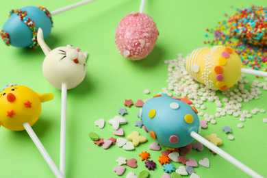 Photo of Delicious sweet cake pops for Easter celebration on green background, closeup