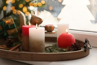 Tray with beautiful burning candles and Christmas decor on windowsill