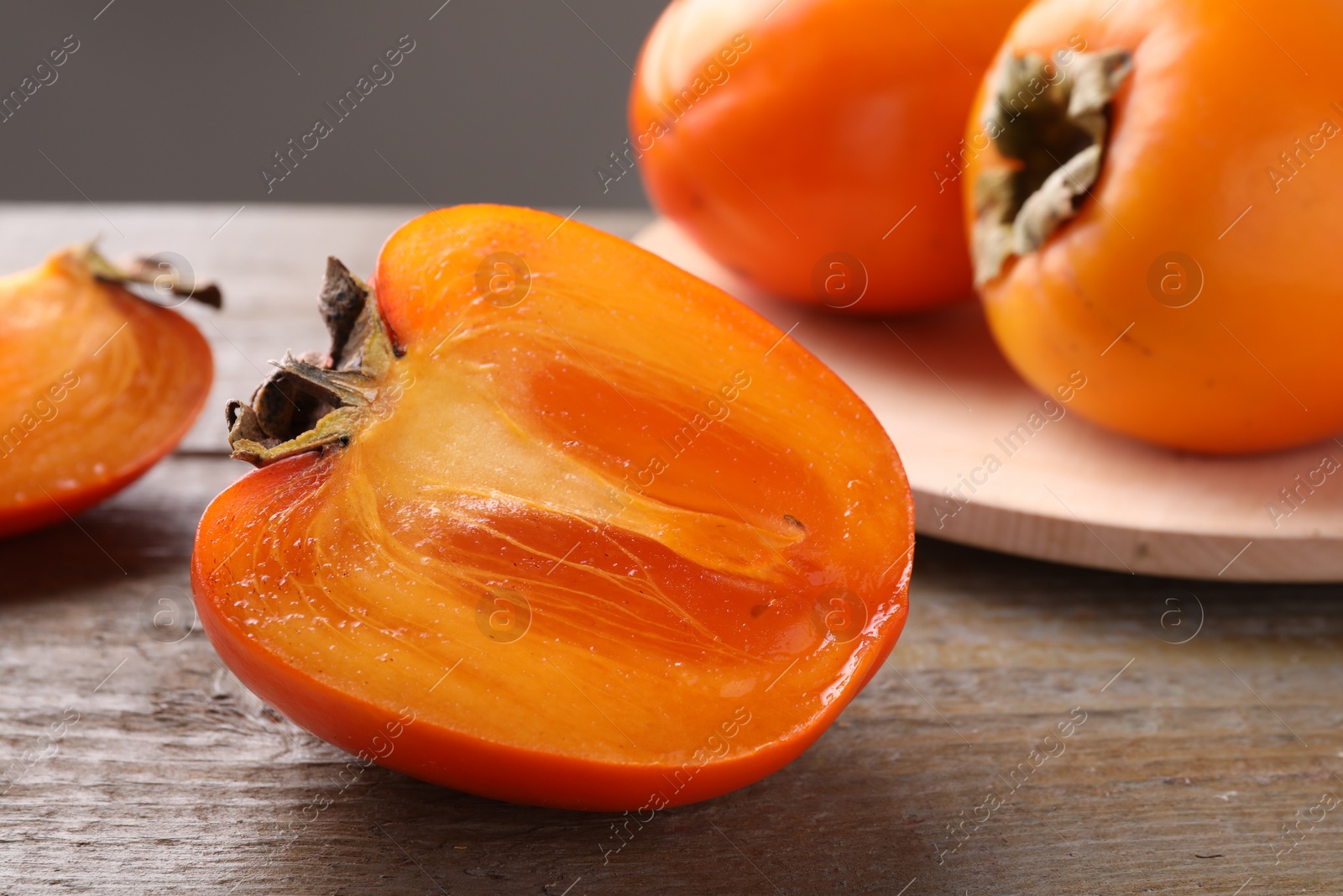 Photo of Whole and cut delicious ripe persimmons on wooden table, closeup