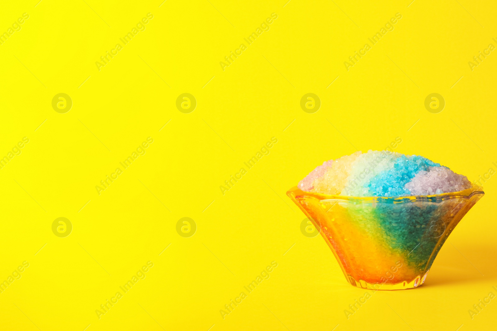 Photo of Rainbow shaving ice in glass dessert bowl on yellow background, space or text