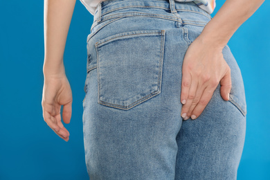 Woman suffering from hemorrhoid on light blue background, closeup