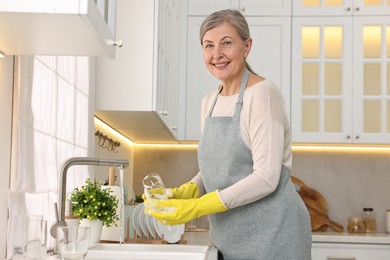 Photo of Happy housewife washing glass in kitchen sink