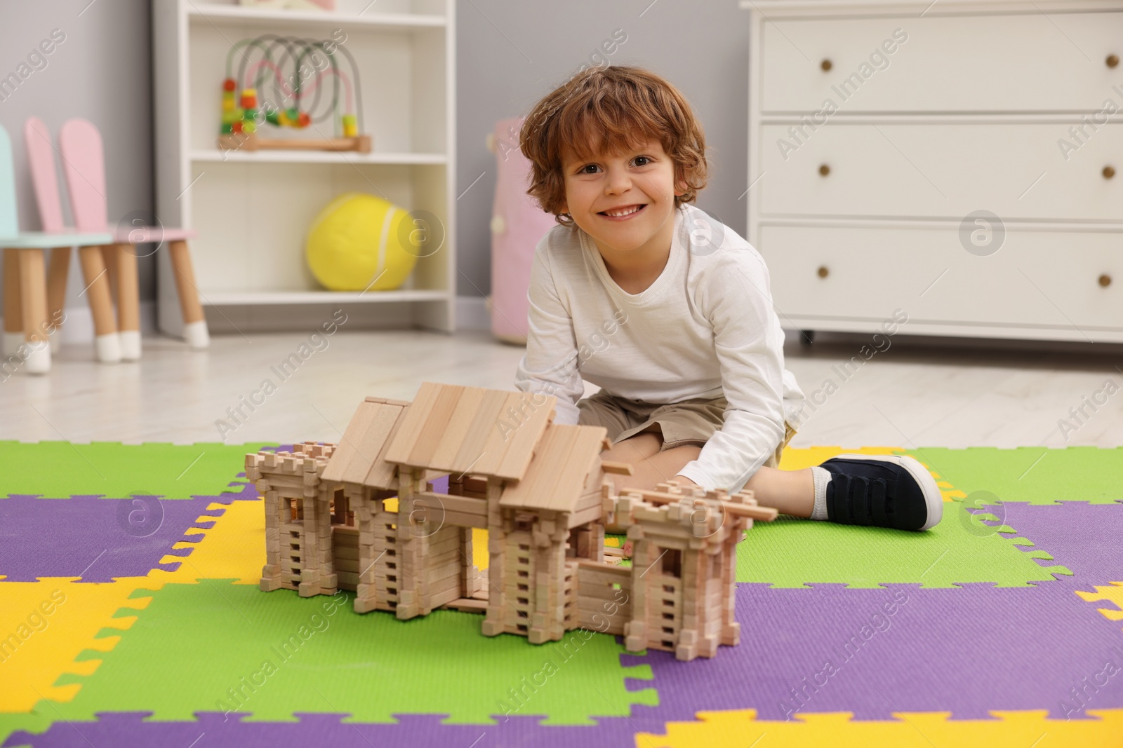 Photo of Little boy playing with wooden entry gate on puzzle mat in room. Child's toy