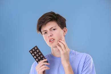 Teenage boy with acne problem holding chocolate on grey background. Skin allergy