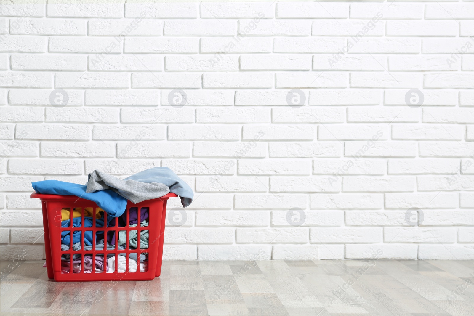 Photo of Red laundry basket with dirty clothes on floor near brick wall. Space for text