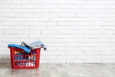 Red laundry basket with dirty clothes on floor near brick wall. Space for text