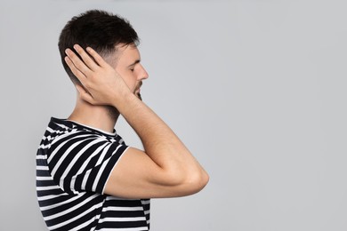 Young man suffering from ear pain on light grey background. Space for text