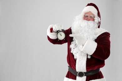 Photo of Santa Claus holding alarm clock on light grey background, space for text. Christmas countdown