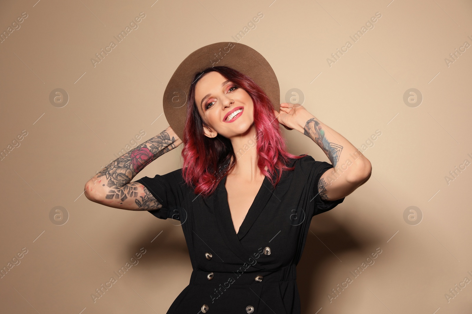 Photo of Beautiful woman with tattoos on arms against beige background