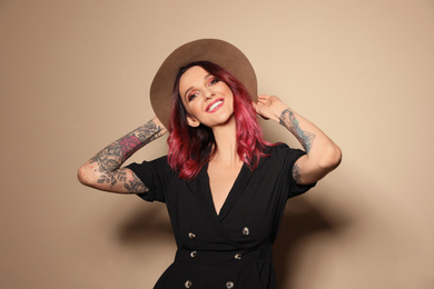 Photo of Beautiful woman with tattoos on arms against beige background