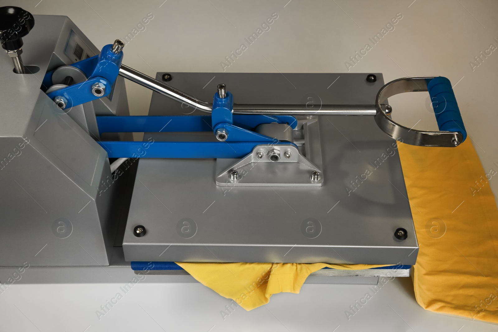 Photo of Printing logo. Heat press with yellow t-shirt on white table