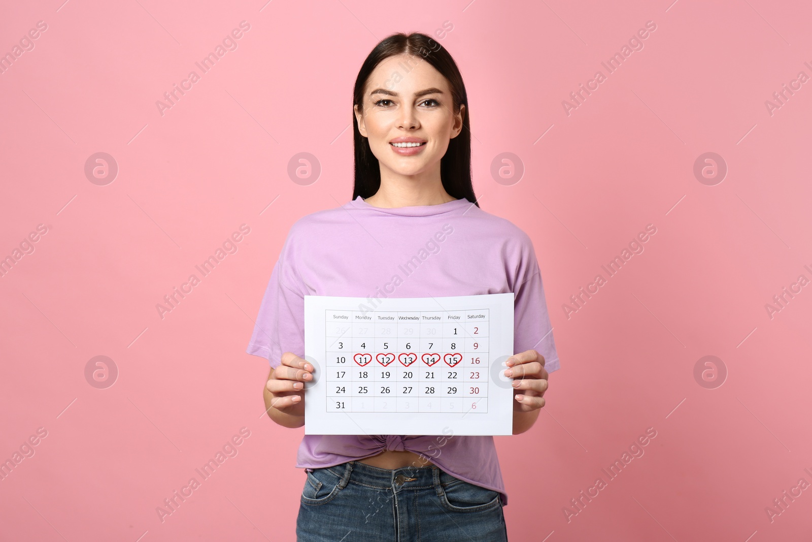 Photo of Young woman holding calendar with marked menstrual cycle days on pink background