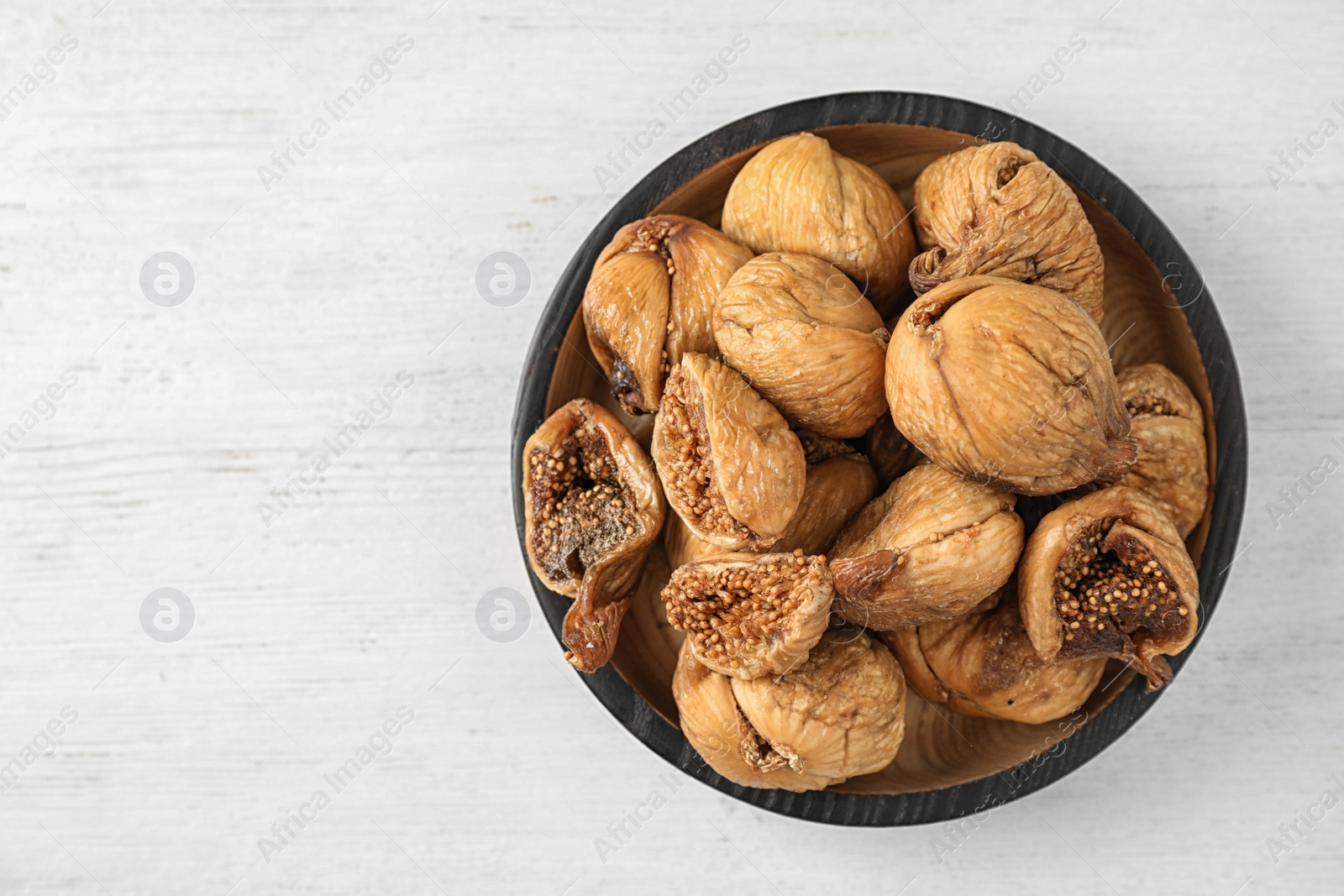 Photo of Wooden bowl of tasty dried figs on white table, top view. Space for text