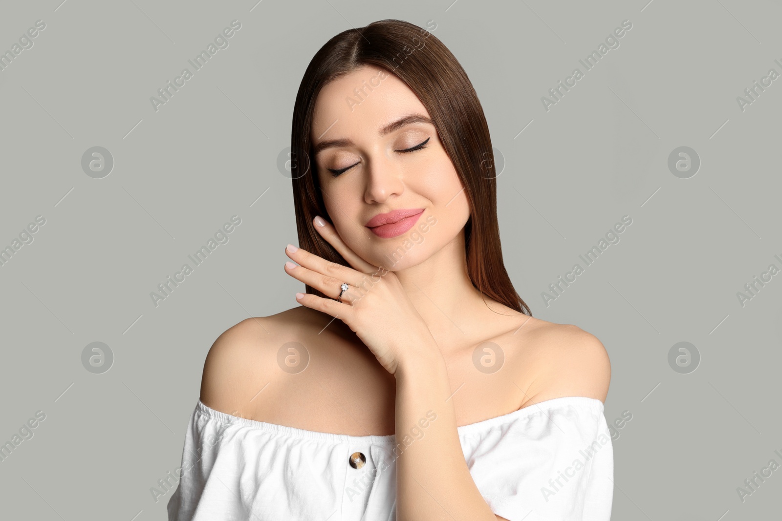 Photo of Happy young woman wearing beautiful engagement ring on grey background