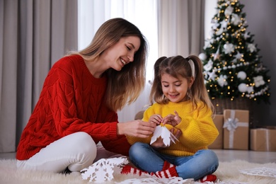Photo of Happy mother and daughter making paper snowflake near Christmas tree at home